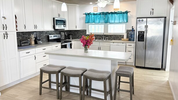Una cocina moderna con armarios blancos, una isla central con taburetes de bar, un refrigerador de acero inoxidable y un ventilador de techo.