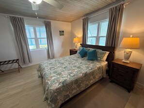 Ein Schlafzimmer mit einem Bett, zwei Nachttischen, einem Fenster mit Vorhängen, einem Deckenventilator und einer Wandlampe.