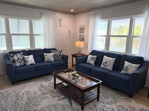 Ein Wohnzimmer mit zwei blauen Sofas, einem Glastisch und einem Teppich mit Muster.