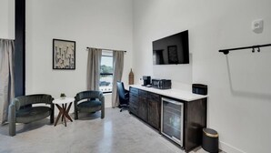 A compact kitchen with a microwave, coffee maker, and a small refrigerator. There are two chairs and a table in the adjacent seating area.