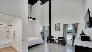 A modern room with a bed, a desk, a chair, a TV, and a window with curtains.