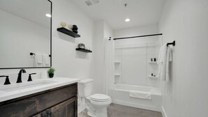 A modern bathroom with a white sink, dark wooden vanity, a white toilet, and a walk-in shower with a black curtain.