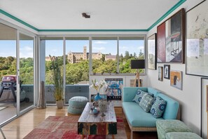 A spacious living room with large windows, a sofa, a coffee table, and a view of a historic building. - Stunning Manly Views | 3BR Coastal Apartment (Manly)