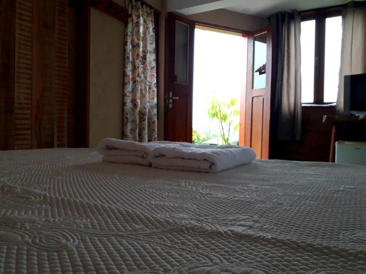 A neatly made bed with folded towels, a wooden door, and a television on a stand.