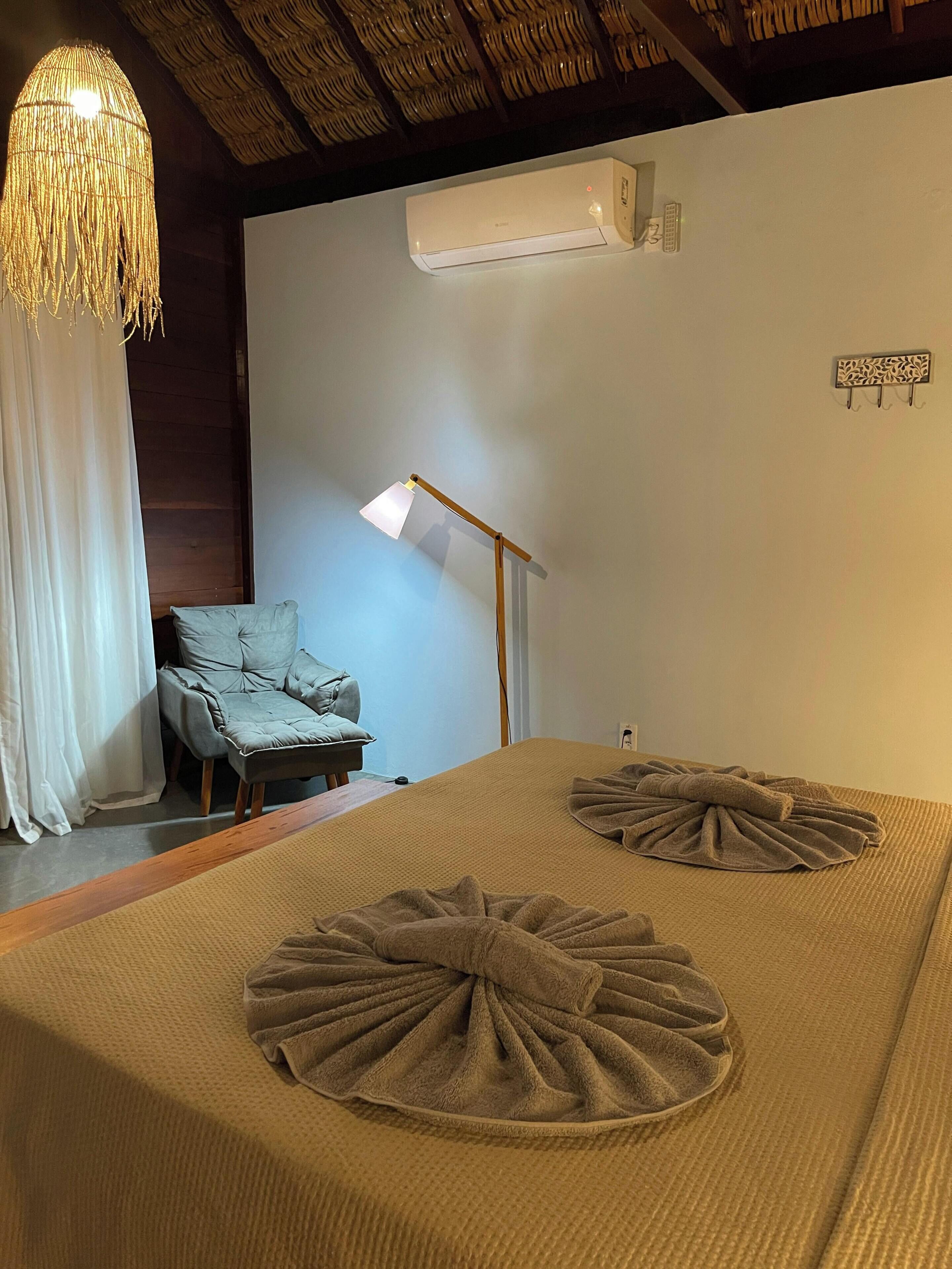 A room with a bed, a chair, a hanging light fixture, and an air conditioning unit.