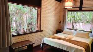 A room with a bed, a nightstand, a lamp, and a window with a view of trees.