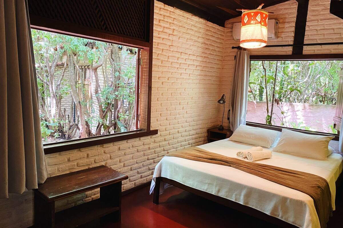 A room with a bed, a nightstand, a lamp, and a window with a view of trees.