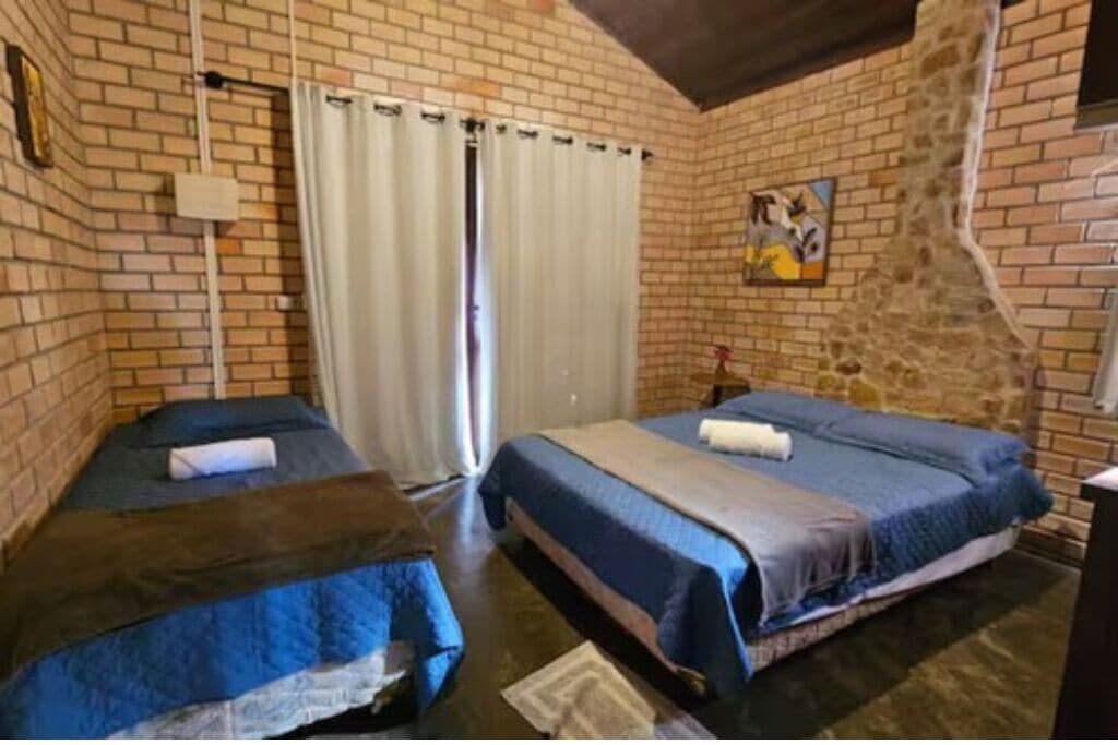A room with two beds, a brick wall, a painting, and a curtain.