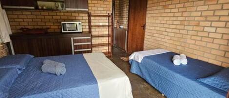 A room with two beds, a microwave, and a brick wall.
