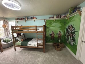 Un letto a castello con un murale a tema foresta, una libreria e una finestra con tende.