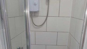 Ein kleiner Duschbereich mit gefliestem Boden, einer Handbrause und einer Bedienkonsole.