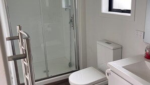 Ein Badezimmer mit Duschkabine aus Glas, einer weißen Toilette und einem Waschbecken mit Fenster darüber.