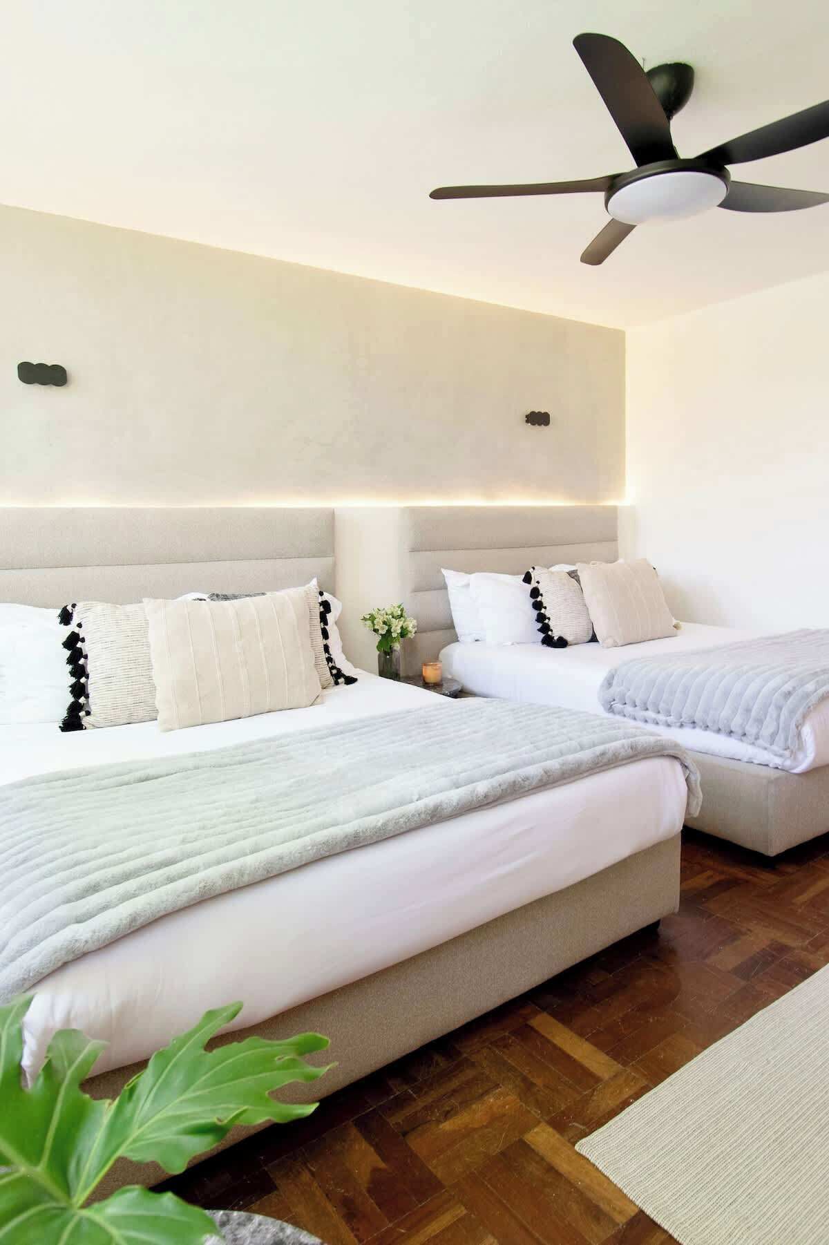A modern bedroom with a large bed, a smaller sofa, a ceiling fan, and a nightstand with a candle.