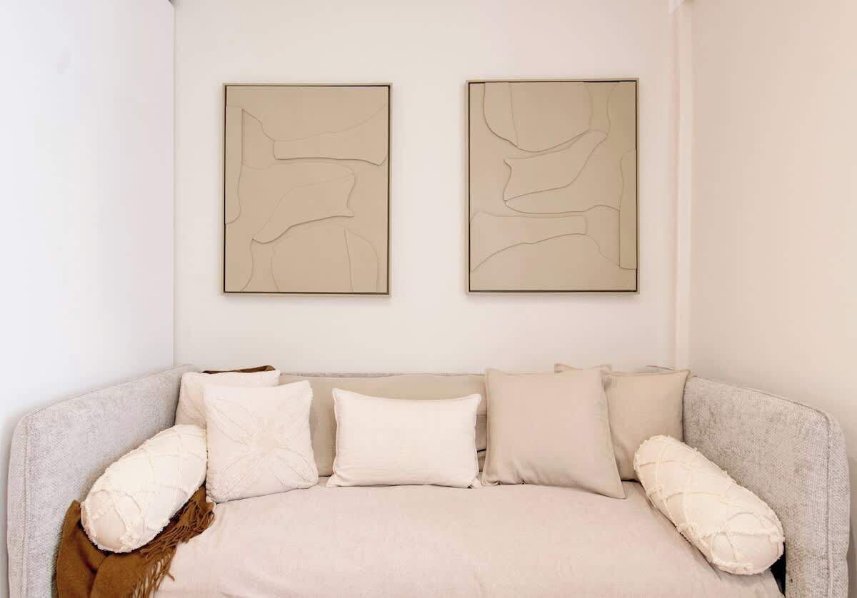 A neutral-toned room with a sofa, two abstract wall art pieces, and a brown throw blanket.
