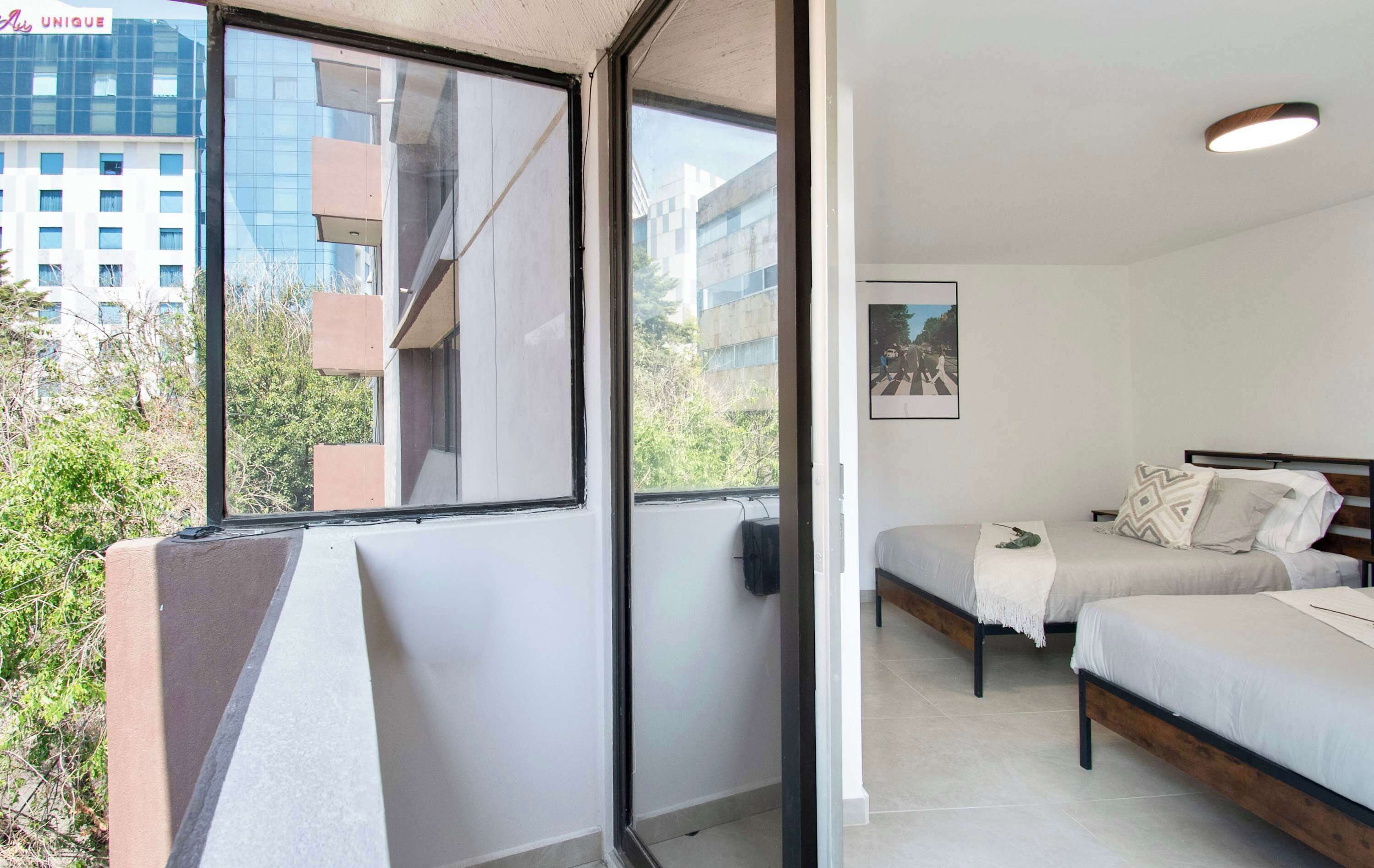 A modern bedroom with two beds, a window, and a view of buildings.
