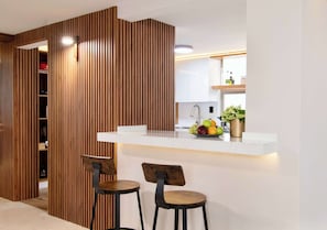 Eine moderne Küche mit weißer Arbeitsplatte, zwei Barhocker und einer Holzwand.