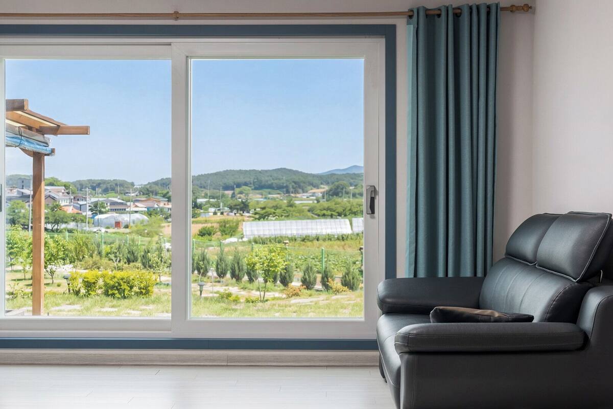 Ein Zimmer mit einer Schiebetür aus Glas, einem schwarzen Ledersofa und Blick auf eine grüne Landschaft mit Gebäuden.