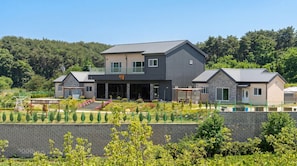 A two-story building with a balcony, a covered patio, and a landscaped garden with various plants and a small pool.