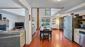 A modern kitchen with a dining area, wooden flooring, and a stone fireplace.