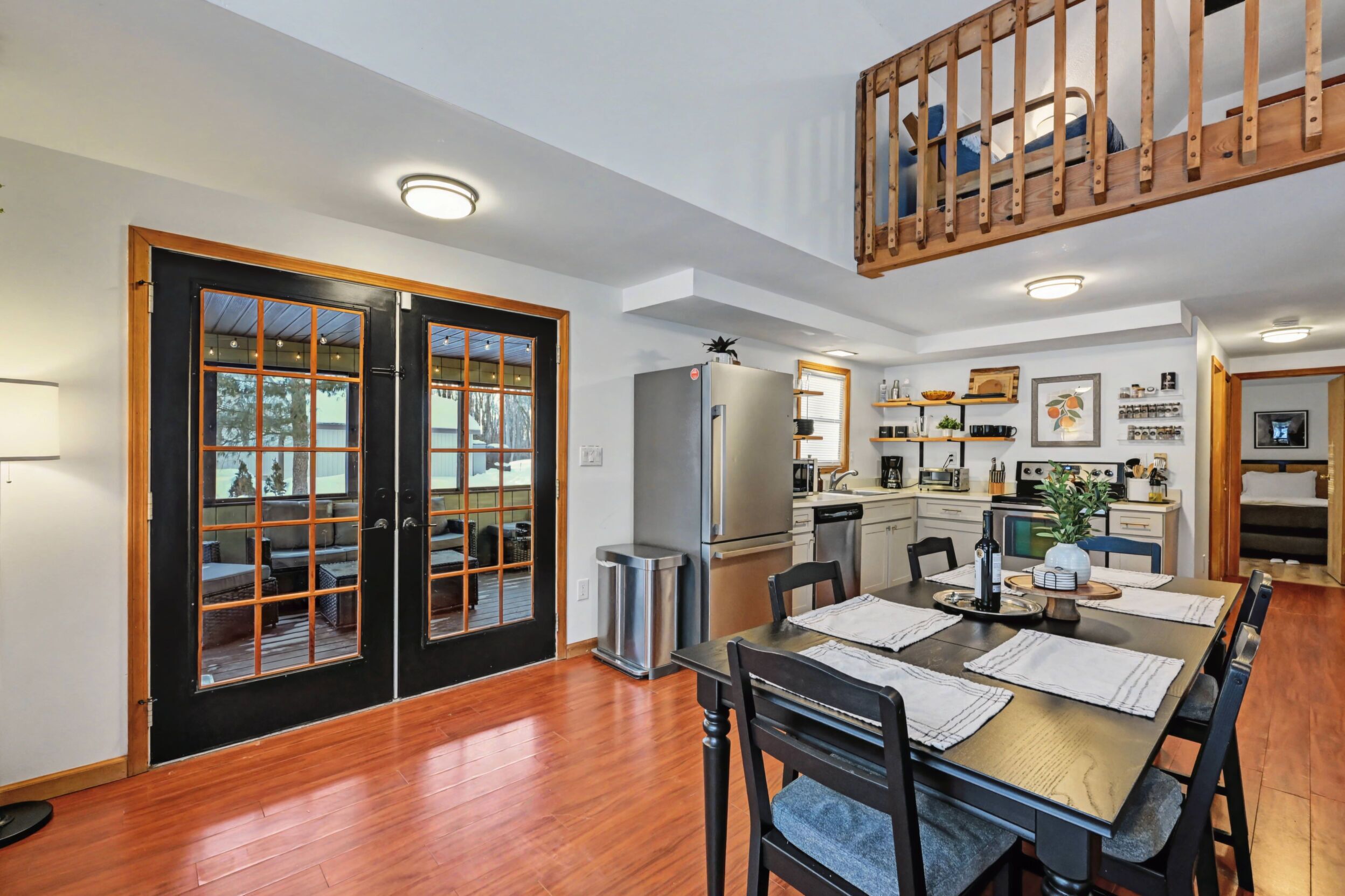 A dining area with a wooden table and chairs, a kitchen with appliances, and a balcony with a wooden railing.