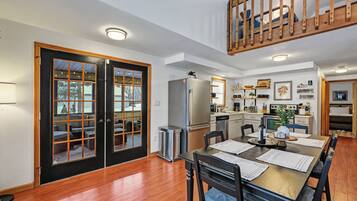 A dining area with a wooden table and chairs, a kitchen with appliances, and a balcony with a wooden railing.