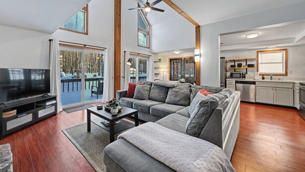 A modern living room with a large flat-screen TV, grey sofas, a coffee table, and a dining area with a kitchen in the background.