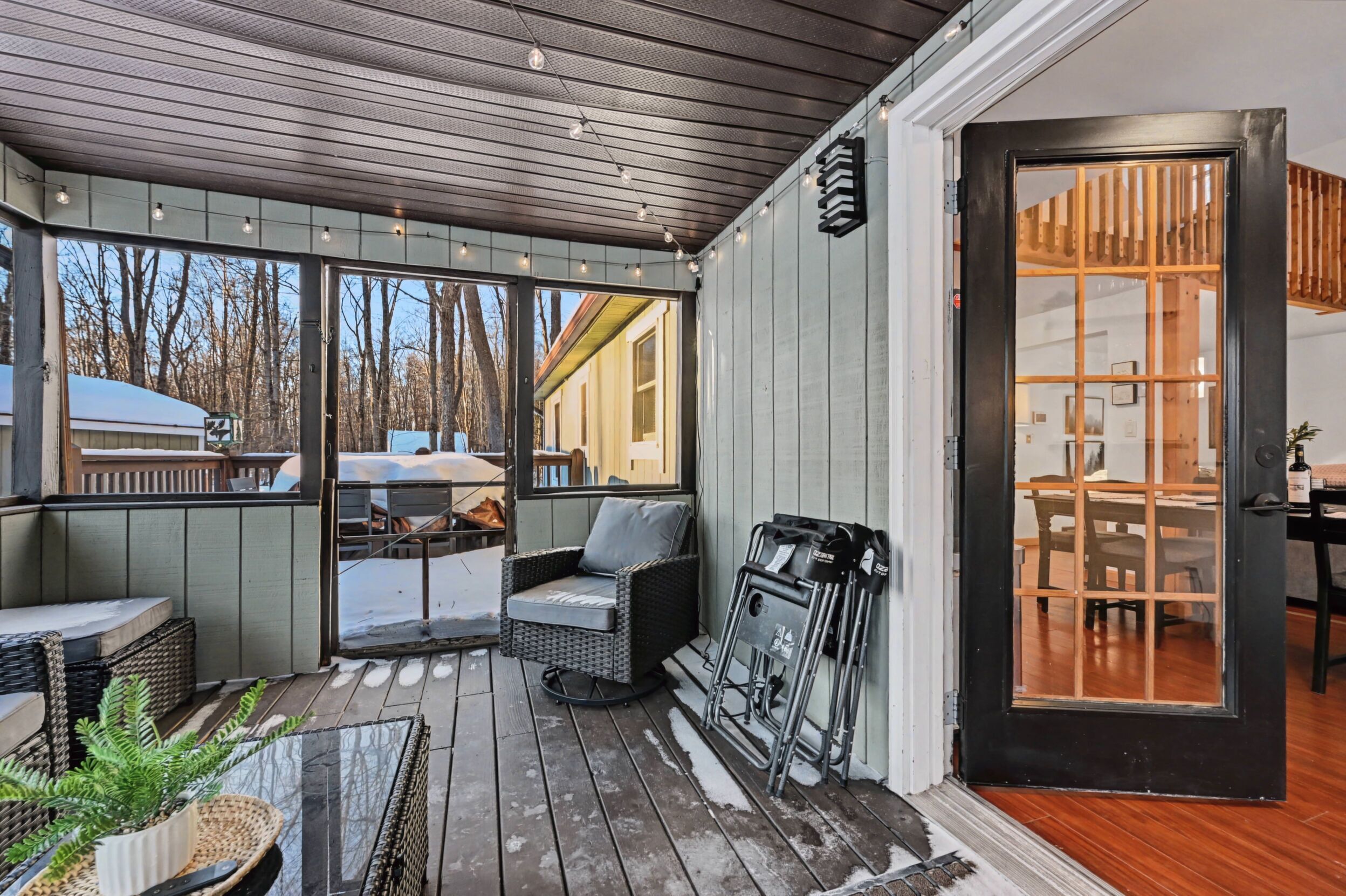 A covered outdoor seating area with wicker furniture, a wheelchair, and a glass door leading inside.