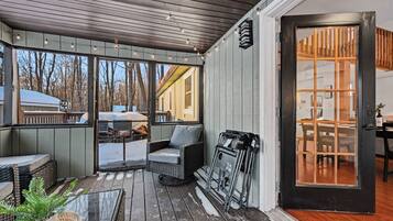 A covered outdoor seating area with wicker furniture, a wheelchair, and a glass door leading inside.