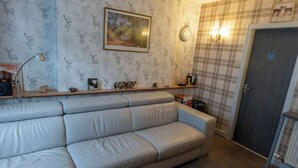 A living room with a sofa, a wall clock, a fireplace, and a door with a sign. - 1BR Charming Cottage in Central Moffat (Moffatt)
