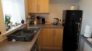 A compact kitchen with wooden cabinets, a black refrigerator, a coffee maker, and a dish rack. - 1BR Charming Cottage in Central Moffat (Moffatt)