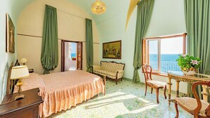 Ein Zimmer mit einem Bett, einem Schlafsofa, einem Esstisch mit Stühlen, einer Pendelleuchte und Meerblick.