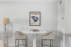 Ein Zimmer mit einem weißen Tisch, zwei Stühlen, einer gerahmten Karte von South Carolina und einer Lampe.