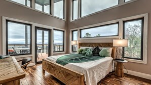 A bedroom with a large bed, multiple windows, a wooden floor, and a view of the outdoors. - Above the Clouds Luxury Retreat with Hot Tub and Epic Views (Morganton)