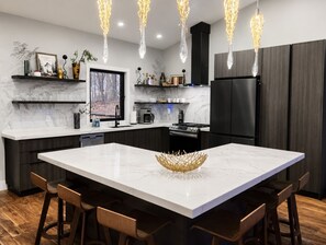 A modern kitchen with a large island, dark cabinetry, and pendant lighting.