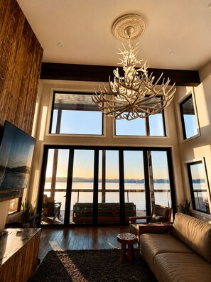 Ein geräumiges Wohnzimmer mit einer großen Chandelier, Holzwänden, einer Couch und Blick auf das Wasser.
