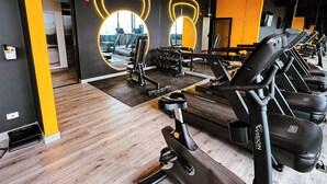 Academia com equipamentos de ginástica, espelho e uma parede amarela.