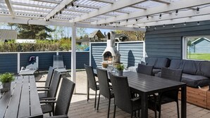 Een terras buiten met een barbecue, zitplaatsen en een pergola.