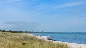 Een strand met een zandstrand, helderblauw water en een verre kustlijn met bomen.
