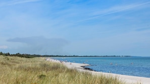 Een strand met een zandstrand, helderblauw water en een verre kustlijn met bomen.