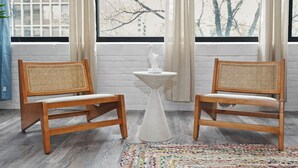 Two wooden chairs with woven backs and white cushions, a white pedestal table, and a colorful rug on a wooden floor.
