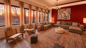 A modern living room with a large window, a sofa set, a rug, and a unique wall art piece.