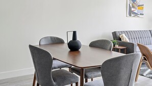 Un comedor con una mesa redonda, sillas tapizadas de gris, un jarrón negro y un sofá gris.