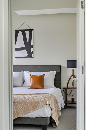 Una cama bien hecha con cabecera gris, una almohada marrón y una manta decorativa.