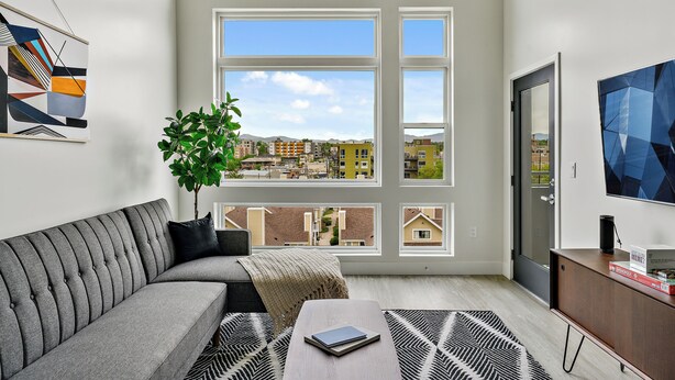 Una sala de estar moderna con un sofá gris, una mesa de centro, una planta en maceta y un ventanal con vistas a la ciudad.