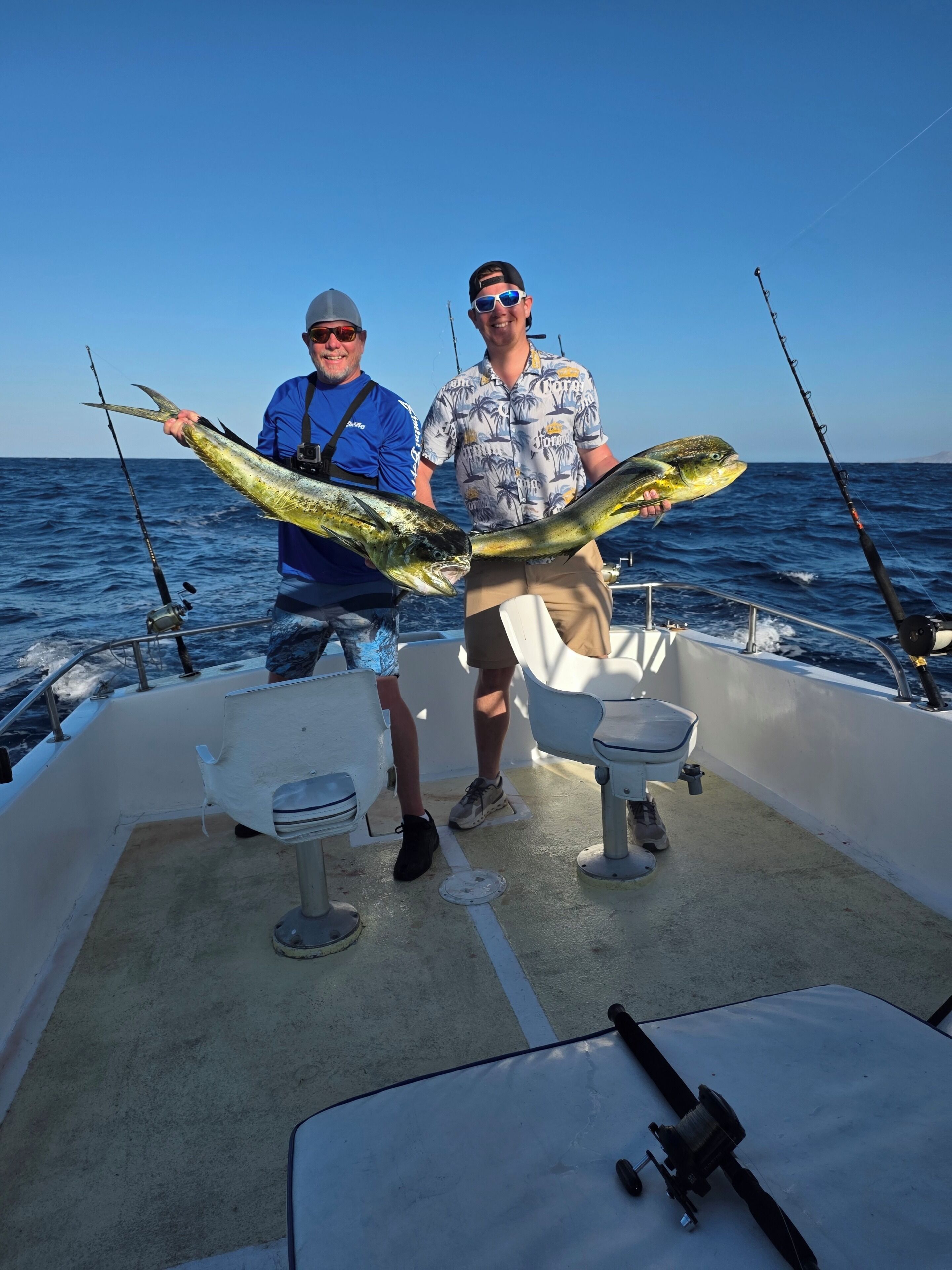 Two people on a boat holding large fish, with fishing rods and a table.