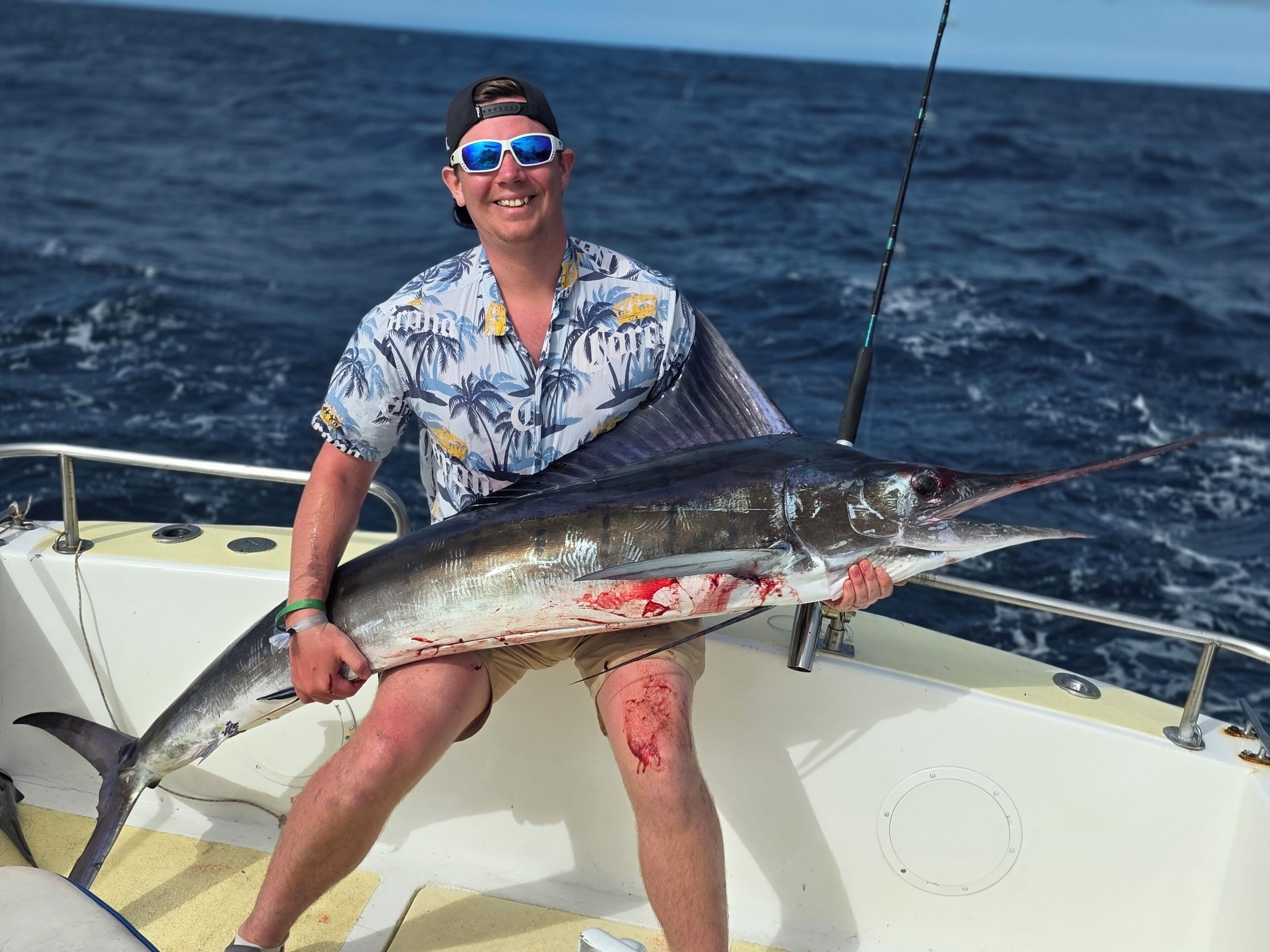 A person holding a large fish on a boat with the ocean in the background.