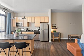 A modern kitchen with a central island, wooden cabinets, stainless steel appliances, and a dining area with a table and chairs. - MSP Voyager | By Childrens Hospital | Free Parking (Minneapolis)