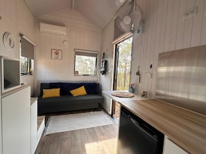 Une cuisine compacte dotée d’un lave-vaisselle encastré, d’une fenêtre offrant une belle vue, d’un petit coin salon avec des coussins et d’un ventilateur fixé au mur.