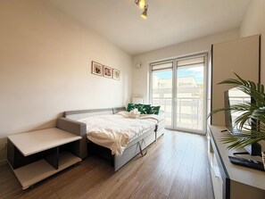 A bedroom with a bed, a desk, a chair, a plant, and a sliding glass door to the outside. - Tarnogaj Modern Apartment (Wrocław)