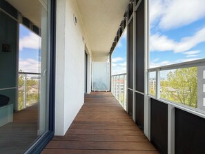 A balcony with a wooden floor, large windows, and a view of buildings and trees. - Tarnogaj Modern Apartment (Wrocław)